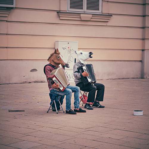 music two person wearing horse heads sitting on folding chairs while playing accordions beside brown concrete building accordion